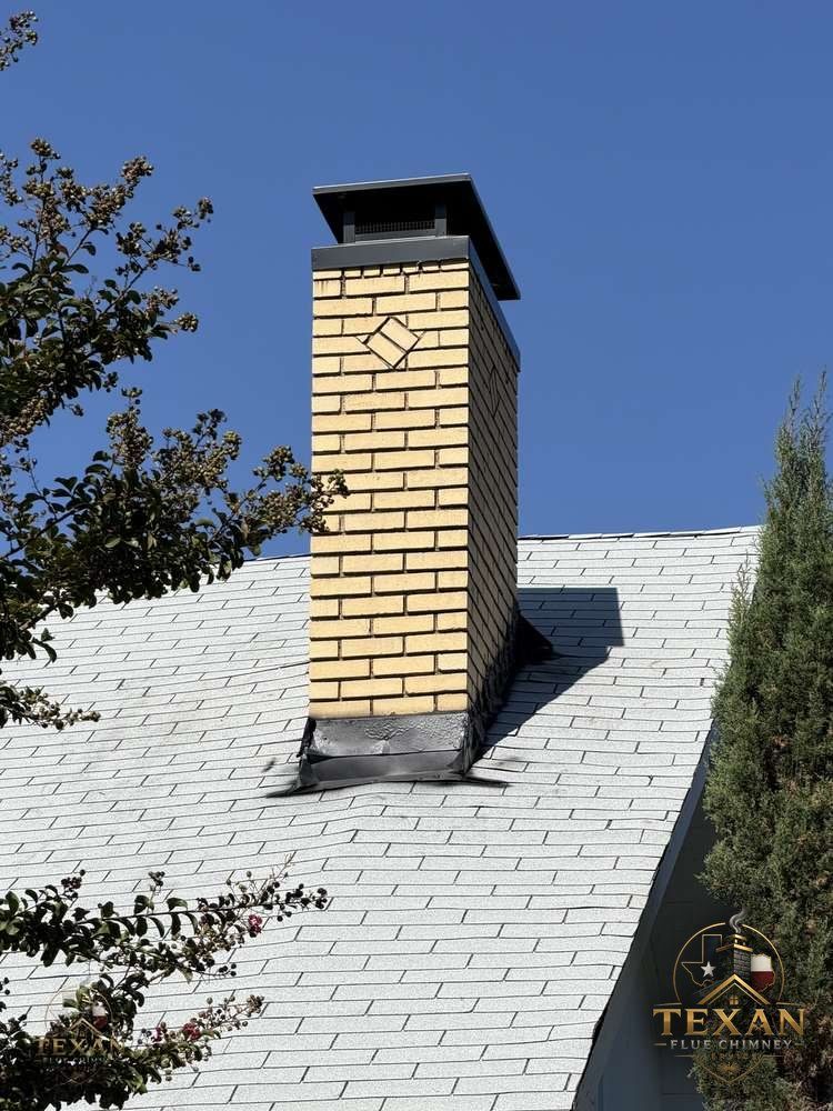 Yellow brick chimney topped with a new powder-coated cap under a Texas blue sky
